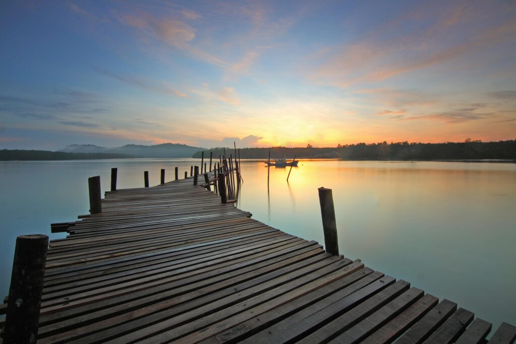 pexels photo 383485 383485 Tranquil sunrise view over a wooden pier with calm water and a distant boat.